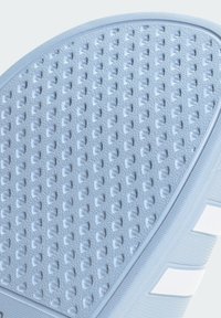 Primer plano de la suela de zapato azul claro con patrón texturizado antideslizante y vista parcial de las franjas blancas en el lateral.