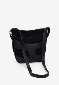 Bolso cruzado de cuero negro y gamuza con acentos redondeados, correa ajustable y textura suave. Diseño minimalista sin marcas visibles.