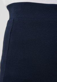 Navy blue ribbed fabric with a smooth texture, featuring a high elastic waistband and side pockets for a fitted silhouette.