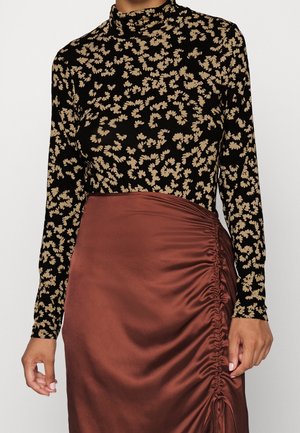 Femme portant un haut à manches longues noir avec des motifs de feuilles beiges et une jupe en satin marron froncée, vue du cou jusqu'au milieu des cuisses.