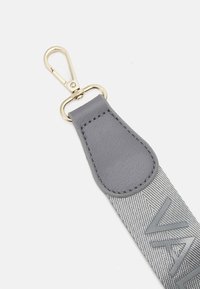 Šedý textilní popruh s texturovaným povrchem, s koženou částí na vrchu. Odolný kovový klip v zlatém tónu pro připevnění.