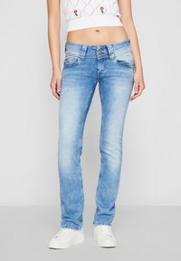 Lys blå denimjeans med rett ben, falmet vask, to frontlommer og knappdetaljering i midjen. Stylet med hvite sko.