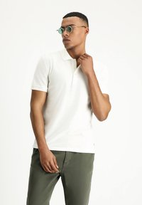 Polo shirt bianco a maniche corte con motivo testurizzato, colletto a tre bottoni e vestibilità slim. Indossato con pantaloni verdi a taglio rilassato.