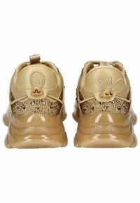 Zapatillas beige con una parte superior brillante y texturizada que presenta detalles decorativos. Material suave, cuello acolchado y una lengüeta que mejoran la funcionalidad.