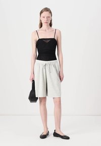 Černý průhledný top bez rukávů, světle šedé šortky na stažení, černé ploché boty, v ruce černá kabelka. Minimalistický design, uvolněný střih, měkké materiály.
