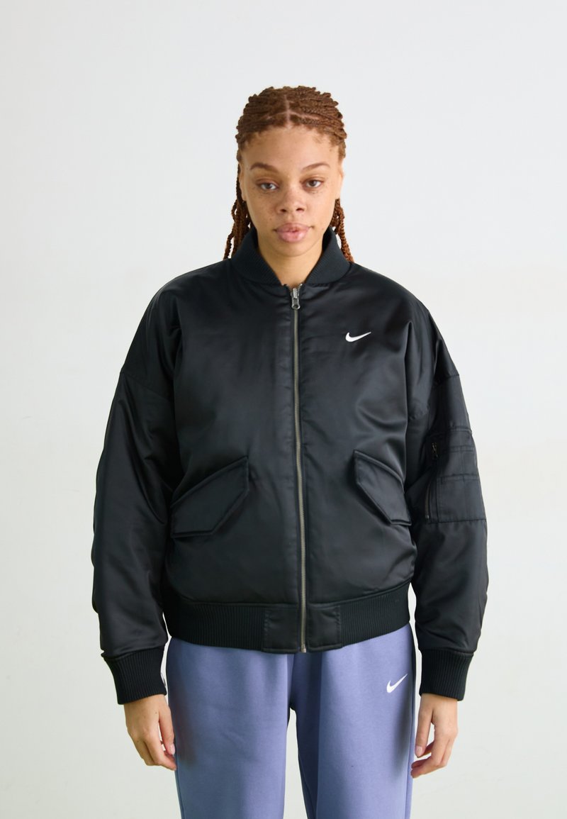 Veste bomber noire avec fermeture éclair, poignets côtelés et deux grandes poches avant. Présente un petit logo Nike blanc sur la poitrine.