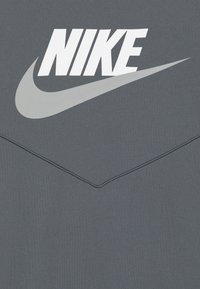 Grå sweatshirt med en stor vit "NIKE"-logotyp och en swoosh-design i ljusare grått. Slät yta med sydda detaljer på sömmarna.