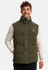 Vesta puf din corduroy verde, cu guler înalt, butoane tip snap și buzunare laterale. Prezintă o eticheta cu logo pe piept și un material texturat.
