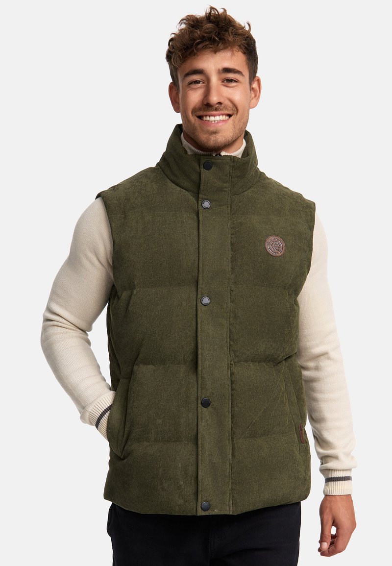 Vesta puf din corduroy verde, cu guler înalt, butoane tip snap și buzunare laterale. Prezintă o eticheta cu logo pe piept și un material texturat.