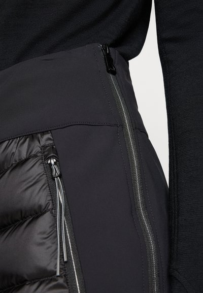 Jupe noire isolée avec un design épuré, un matériau lisse, un motif matelassé horizontal et une quincaillerie en zip argentée contrastante.