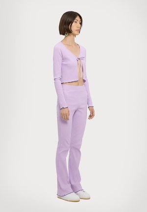 Lilla ribbet strikket crop top med frontknute og flagrende bukser med volangkant. Kombinert med hvite sko. Glatt tekstur.