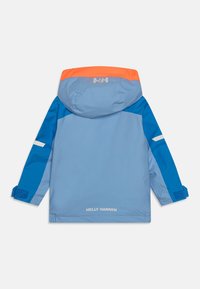 Mėlyna nepralaidi vandeniui striukė su oranžine kapišonu, atspindinčiais akcentais, Velcro rankogaliais ir Helly Hansen logotipu ant nugaros ir rankovės.
