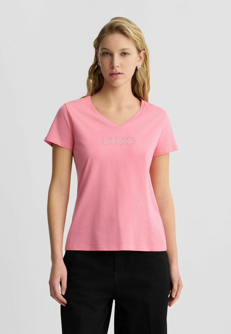 Rosa Baumwoll-T-Shirt mit V-Ausschnitt und kurzen Ärmeln, versehen mit einem dekorativen Logo aus Strasssteinen auf der Vorderseite. Einfaches und tailliertes Design.