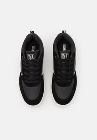 Sneakers neri realizzati con una combinazione di pelle liscia e suede testurizzato, con suola bianca e lacci neri. Dettaglio del logo ben visibile sulla linguetta.