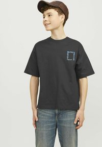 Camiseta de algodón negra de manga corta, con texto gráfico azul en el lado izquierdo del pecho, combinada con jeans de mezclilla azul claro.