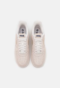 Pink suede sneakers with white laces, perforated toe, gold logo accents, and a textured rubber sole. Flat design with cushioned interior.