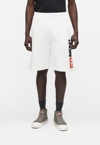 Weiße Baumwollshorts mit einem Tunnelzugbund und einem schwarzen und roten "DIESEL"-Logo an der Seite, kombiniert mit grauen High-Top-Schuhen und dunklen Socken.