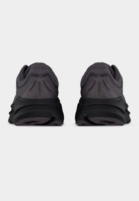 Ζευγάρι αθλητικών παπουτσιών σκούρου γκρι με παχιά μαύρη σόλα, εμφανιζόμενα από πίσω, με το κείμενο "BONDI 9" στη φτέρνα.