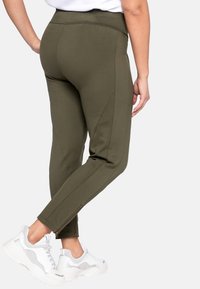 Pantaloni aderenti color verde oliva in tessuto elasticizzato, con zip alla caviglia. Abbinati a sneakers bianche, per un look casual.
