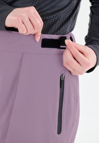 Lila vattentäta byxor med en dragkedjeficka och justering av midjan med kardborreband, med slät textur och skräddarsydd passform.