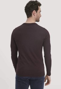 Bordeauxfarbener Strickpullover mit langen Ärmeln, Rundhalsausschnitt und gerippten Bündchen. Die Textur erscheint glatt mit einer figurbetonten Silhouette.