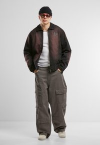 Svart og rød gradientjakke med krage, kombinert med løse, beige cargo-bukser med sidelommer og hvite sneakers. Tilbehør inkluderer solbriller og en lue.