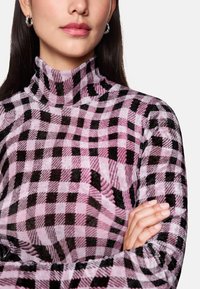 Turtleneck sweater featuring a pink and black checkered pattern with a textured fabric. Fitted design with a high collar and long sleeves.