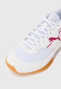 Hvite treningssko med mesh-overdel, gummisåle og en rosa Puma-logo. Teksturert design med ton-i-ton snøringer og rund tå.