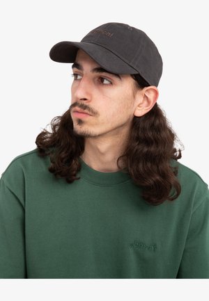 Grijze baseballcap met een gebogen rand en geborduurd logo. Ggedragen met een groene sweatshirt met een subtiel, tonale logo op de borst.