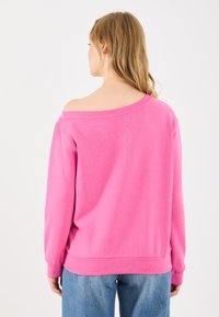 Lys rosa sweatshirt med avtagende skuldre-design, ribbede mansjetter og nederkant. Mykt, teksturert stoff; avslappet passform.