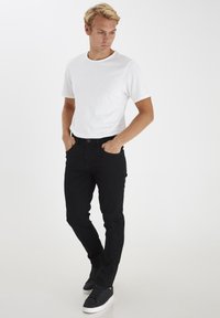 Witte T-shirt met korte mouwen gecombineerd met zwarte slim-fit jeans en zwarte sneakers met witte zolen. Eenvoudig, modern ontwerp met een klassieke snit.