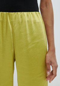 Limoengroene broek met een gestructureerde afwerking en elastische tailleband, gecombineerd met een zwart geribbeld topje, dat een gladde stof en een ontspannen fit laat zien.