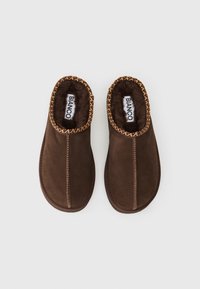 Brune ruskinds slippers med blødt for. Har fletdetaljer langs åbningen og kontrasterende syninger langs kanterne.