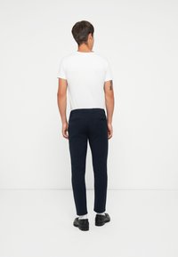 Navy maßgeschneiderte Hose mit schmalem Schnitt, glatter Textur, elastischem Bund und Gesäßtaschen. Kombiniert mit einem schlichten weißen T-Shirt mit kurzen Ärmeln.