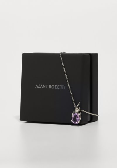 Colier argintiu cu un pandantiv în formă de pere, dintr-o piatră prețioasă purpurie, prezentat într-o cutie mată neagră cu numele brandului "ALAN CROSETTI" afisat.