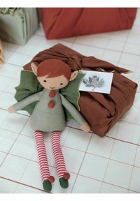 Zachte stoffen pop met groene vleugels, een grijze jurk, rode knopen en gestreepte benen. Naast een bruin, ingepakt cadeau met een decoratief label.