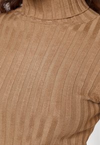 Maglione a collo alto in tessuto a costine, di colore marrone chiaro. Presenta un collo alto e un design aderente, che mette in risalto la texture del materiale.