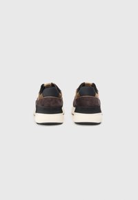 Sneakers featuring a combination of brown suede and black leather, with a white and black rubber sole, and minimalistic design details.