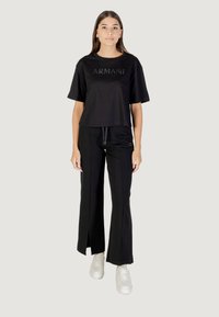 Camiseta negra corta con logo de strass "ARTHUR", combinada con pantalones anchos negros con aberturas y zapatillas blancas.