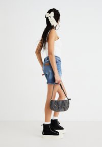 Jeansen, vit linnen, svarta högklackade sneakers med vit sula och en grå handväska med gyllene nitar. Håret stylat med en stor vit rosett.
