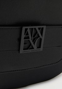 Μαύρη τσάντα από δερματίνη με υφή, με μαύρη μεταλλική πλακέτα λογότυπου Armani Exchange, με ανάγλυφα τα γράμματα "AX" και το όνομα της μάρκας.