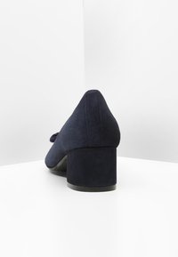 Marina mockaskor med klack, med en slät yta, rund tå och dekorativ rosett framtill.