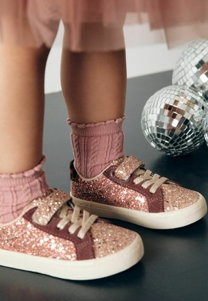 Glittriga rosa och bruna sneakers med kardborreband, i kombination med ribbade rosa strumpor. Bakgrunden har små discokulor.