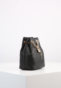 Borsa a secchiello in pelle nera con superficie testurizzata, dettaglio con catena dorata e chiusura a lucchetto. Chiusura con lacci nella parte superiore. Base rotonda.