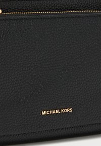Fekete bőr pénztárca texturált felülettel, aranyszínű fémalkatrészekkel és az elülső oldalán látható, dombornyomott "MICHAEL KORS" márkanévvel.