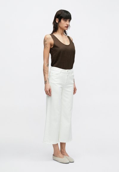 Άσπρο κοντό παντελόνι με φαρδιά μπάτζα, σε συνδυασμό με καφέ αμάνικη μπλούζα. Το ύφασμα φαίνεται απαλό με λεία υφή. Το σύνολο είναι απλό και casual.