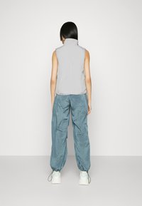 Ljusgrå ärmlös väst kombinerad med lösa, krusade tealbyxor. Vita sneakers med mintgröna detaljer. Minimalistisk design, mjukt material.