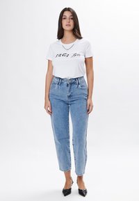 Hvid bomulds t-shirt med sort grafisk tekst, parret med lyseblå højtaljede denimjeans. Sorte spidse slingback sko.