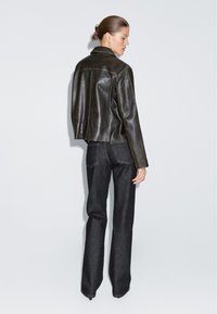 Giacca di pelle marrone con un design strutturato, colletto alto e vita aderente. Abbinata a jeans in denim scuri a gamba svasata.