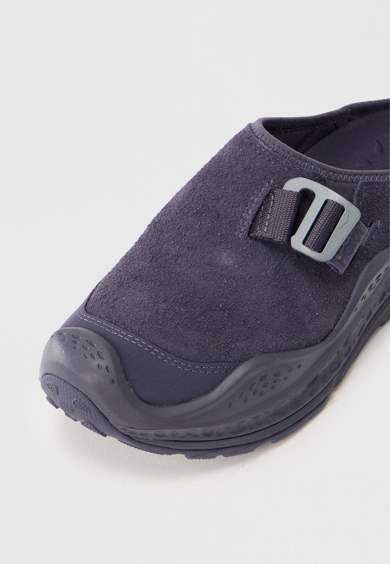 Zapato azul marino tipo slip-on con parte superior de ante texturizado, detalle de hebilla de plástico y suela de goma duradera con agarre estampado.